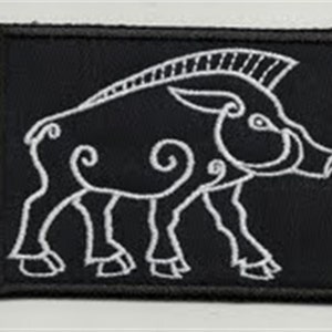 Peut inclure: Un écusson brodé noir avec un contour blanc d'un sanglier ou d'un cochon sauvage stylisé. Le sanglier a une queue recourbée et une crête sur la tête.