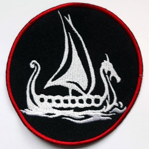 Puede incluir: Un parche bordado blanco de un barco vikingo con una vela sobre un fondo negro con un borde rojo.