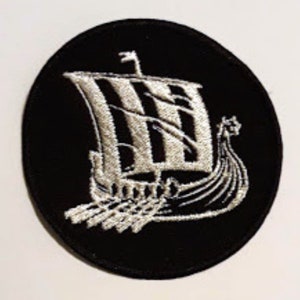 Puede incluir: Un parche bordado negro con un diseño de barco vikingo blanco. El barco tiene una vela con rayas verticales y una proa puntiaguda.