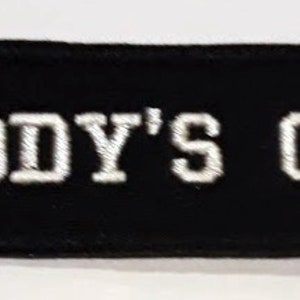 May include: Black fabric patch with white embroidered text that reads "DADDY'S GIRL".