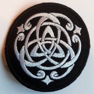 Puede incluir: Un parche circular negro con un diseño de nudo celta bordado en blanco.