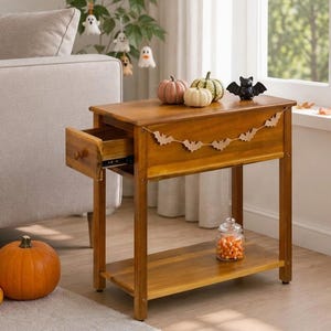 May include: A rectangular wooden side table with a warm brown finish, featuring a single pull-out drawer on the left side and an open bottom shelf. The table is decorated with a small paper bat garland and holds three small pumpkins and a black bat.