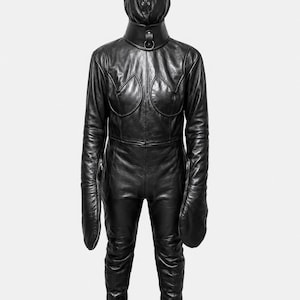 May include: A black leather full-body suit featuring a hood that covers the head, a high collar with a metal ring attachment, long sleeves with integrated mitten-like hand coverings, and decorative curved paneling across the chest area.
