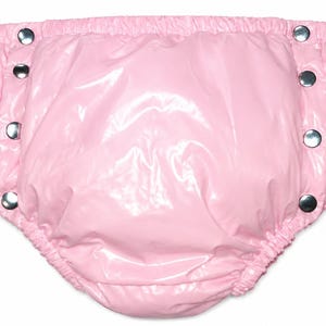 May include: A pair of light pink plastic diaper covers featuring a glossy, shiny finish. The garment has an elasticized waistband and leg openings, with three silver-toned metal snap buttons on each side for closure and adjustment.