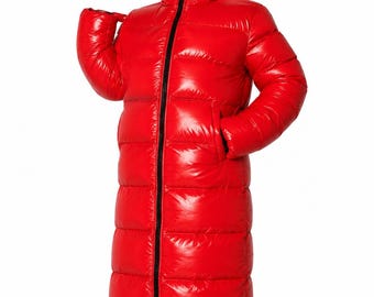 May include: A long, bright red puffer coat with a glossy finish, featuring horizontal quilted channels, long sleeves, and an integrated hood. A prominent black zip runs vertically down the centre front, extending from the hem to the top of the hood.
