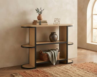 May include: A console table with a light wood finish and a black metal frame. The unit features three horizontal shelves with rounded ends. The top shelf holds a small vase with dried flowers and a stack of books. A dark vase sits on the middle shelf.