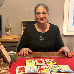 Puede incluir: Una colecci&oacute;n de cartas de tarot dispuestas sobre un mantel rojo. Las cartas presentan diversas ilustraciones coloridas y texto en turco. Un soporte de madera para cartas de tarot se encuentra a la izquierda y un mazo est&aacute; extendido horizontalmente.