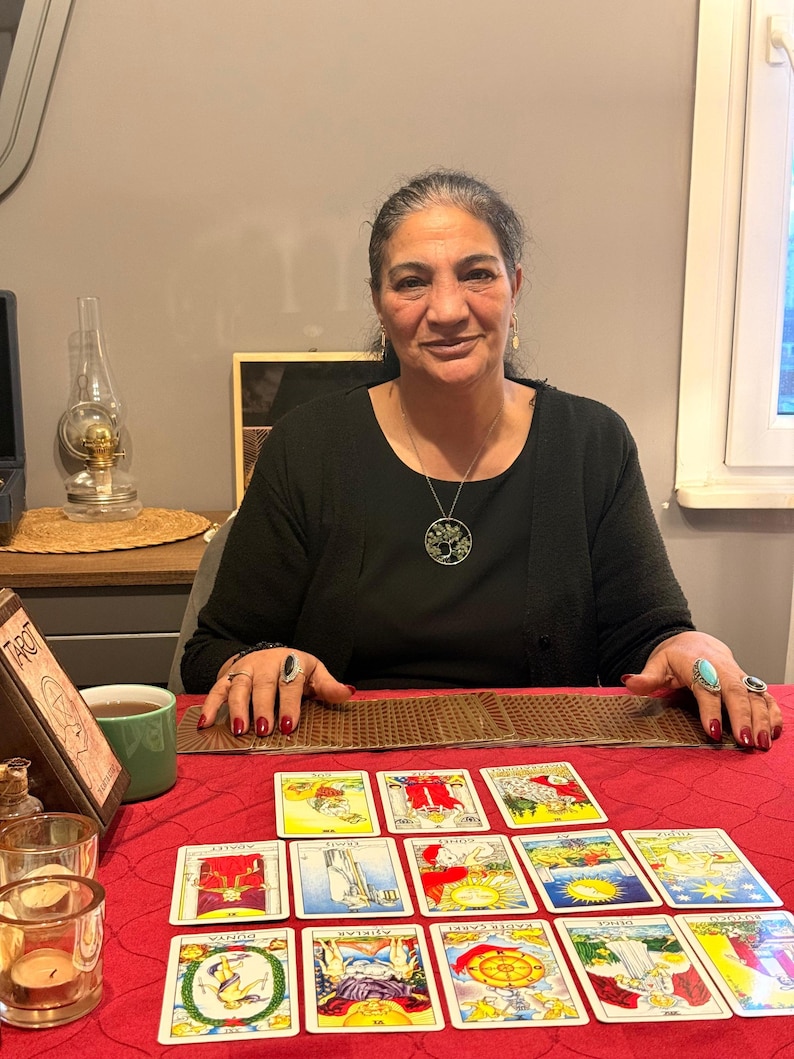 Puede incluir: Una colecci&oacute;n de cartas de tarot dispuestas sobre un mantel rojo. Las cartas presentan diversas ilustraciones coloridas y texto en turco. Un soporte de madera para cartas de tarot se encuentra a la izquierda y un mazo est&aacute; extendido horizontalmente.