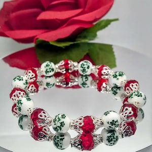 May include: A white and green floral patterned beaded bracelet with red crystal beads and silver accents.