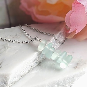 May include: A silver chain necklace with a pendant made of stacked, light blue sea glass.