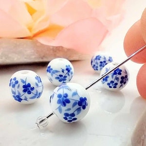 Round Blue Flower Beads hung on silver pin. pink flower in background.