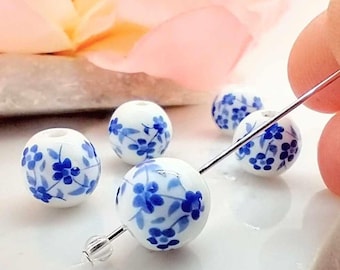 May include: White ceramic beads with a blue floral pattern. The beads are round and have a smooth finish.