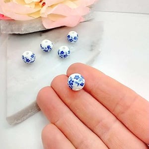 Hand holding 10mm round Blue ceramic flower beads.