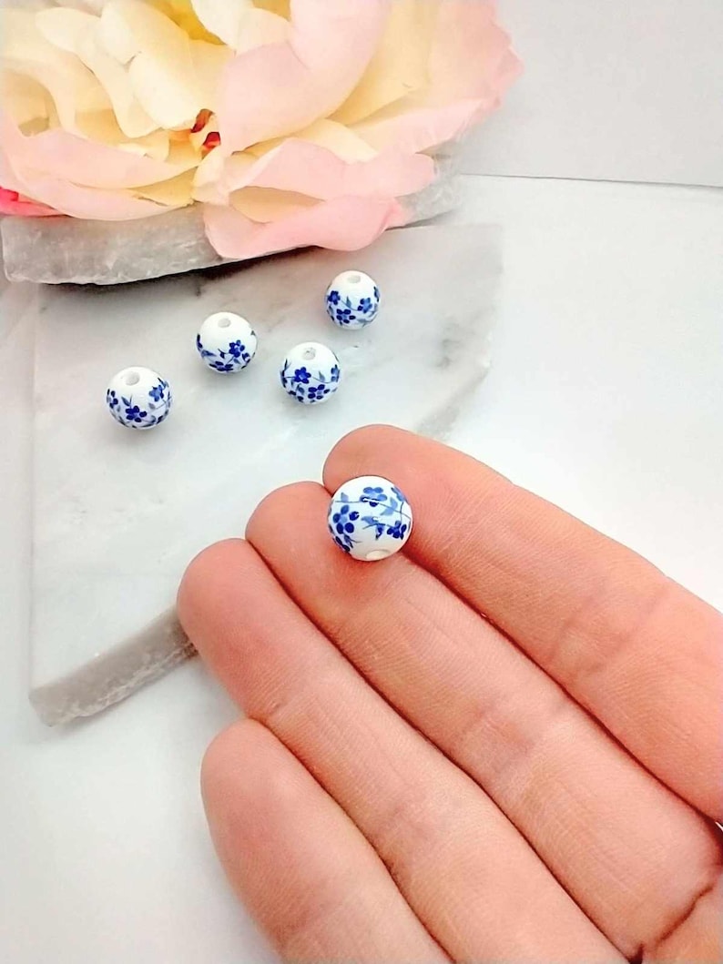 Hand holding 10mm round Blue ceramic flower beads.