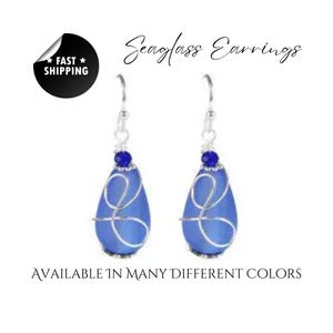 May include: Seaglass earrings with a blue teardrop-shaped stone wrapped in silver wire. The earrings have a small blue bead at the top of the wire.