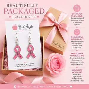 May include: A pair of silver-toned hook earrings featuring a pink ribbon charm with the word HOPE embossed on the front. The earrings are displayed on a white card inside a brown gift box with a pink ribbon, accompanied by a pink flower.