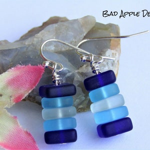 May include: A pair of silver dangle earrings with a stack of blue and white glass beads. The beads are in shades of blue, white, and light blue.