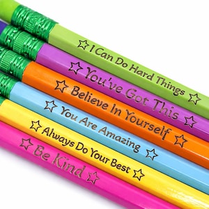 May include: A collection of colorful pencils with motivational phrases and star graphics. The pencils are in shades of green, purple, orange, blue, yellow, and pink. Each pencil has a different message, such as "I Can Do Hard Things" and "Be Kind."