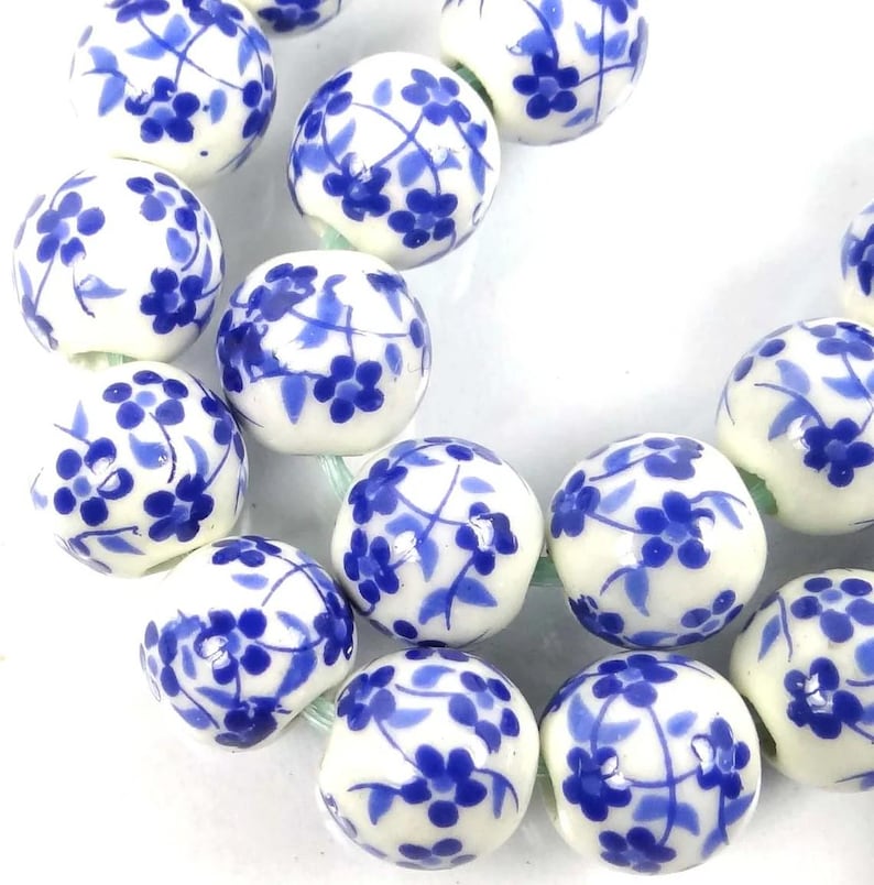 May include: A strand of white ceramic beads with a blue floral pattern. The beads are round and have a glossy finish.