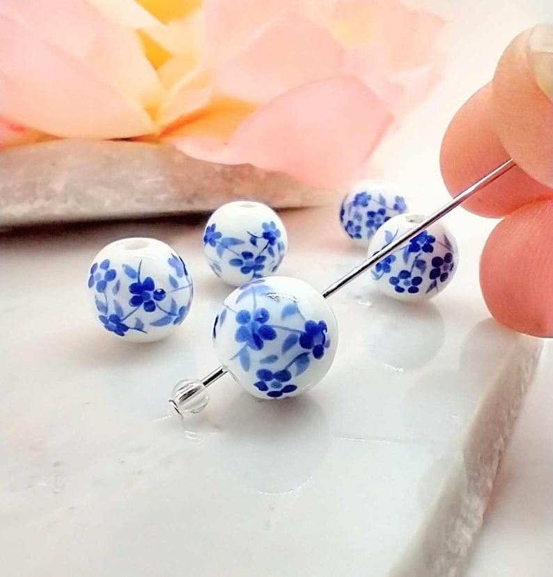 Round Blue Flower Beads hung on silver pin. pink flower in background.