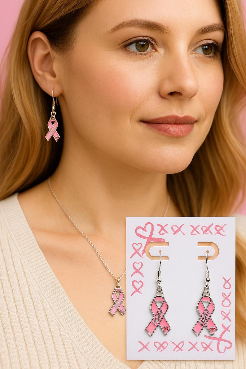 May include: A silver-toned necklace and earring set featuring pink ribbon pendants. Each ribbon charm is enameled in light pink with the word HOPE and a small heart detail. The earrings are displayed on a white card decorated with pink ribbon and heart illustrations.