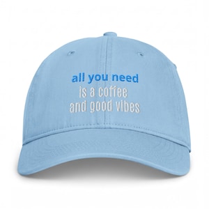 Pode incluir: Um boné de beisebol azul claro com texto bordado na frente que diz all you need em letras azuis, seguido por is a coffee and good vibes em letras brancas. O boné tem uma coroa estruturada, uma aba curva e um botão no topo.