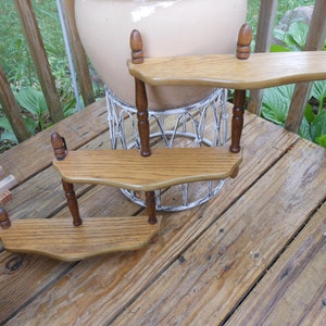 May include: Three wooden shelves with decorative turned spindles, mounted on a wall. The shelves are stained in a light brown color and have a slightly curved shape.