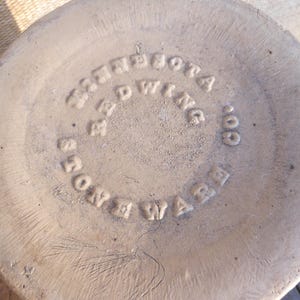 May include: Close-up of the bottom of a stoneware piece with the embossed text "Minnesota Red Wing Co. Stoneware" in a circular pattern. The piece has a light beige color and a textured surface.