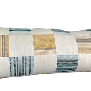 May include: Long rectangular cushion with a patchwork design. The cushion features squares of various colours, including blue, beige, and gold, with striped and textured patterns. Ideal for home decor.