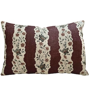 May include: A rectangular throw pillow featuring alternating vertical stripes. The wider stripes are a solid deep burgundy color, while the narrower stripes are cream-colored with a repeating floral pattern in shades of green, brown, and red.