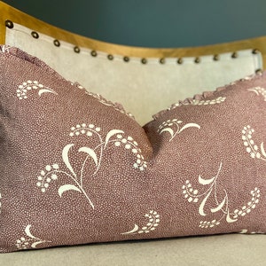 May include: A decorative throw pillow with a pink background and a white floral pattern. The pillow has a ruffled edge.
