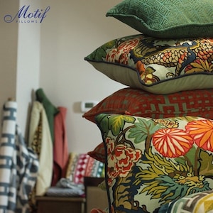 May include: A stack of colorful decorative pillows with floral and geometric patterns. The pillows are arranged in a pyramid shape, with the top pillow being a solid green color. The pillows are made of a variety of fabrics, including cotton, linen, and velvet. The pillows are all different sizes and shapes. The pillows are all in focus, and the background is blurred. The text "Motif Pillows" is visible in the top left corner of the image.