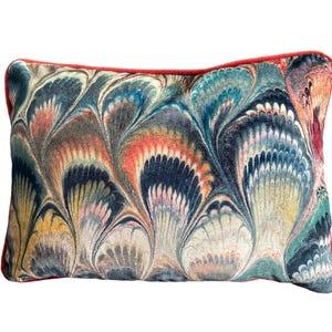 May include: Rectangular decorative pillow with a vibrant, abstract pattern in shades of blue, orange, and yellow. The pillow has a red border, adding a contrasting accent to the colorful design. The pattern resembles a stylized feather or floral motif.