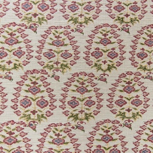 May include: Cream-colored fabric with a repeating floral pattern. The design features clusters of red and blue flowers with green leaves, arranged in an oval shape. The background has a textured appearance.