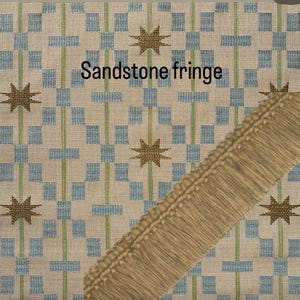 May include: Sandstone fringe with a woven pattern of blue squares and green lines, accented by starburst designs. A tan fringe is shown diagonally across the image. The text "Sandstone fringe" is displayed.