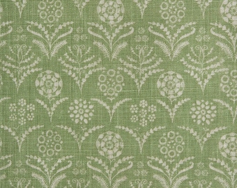 Op de afbeelding: Een saliegroene stof met een herhalend wit bloemenpatroon. Het ontwerp bestaat uit gestileerde ronde bloemhoofdjes en delicate bladstelen die in een symmetrische, verticale opstelling zijn geplaatst. Het textiel heeft een zichtbare geweven textuur.