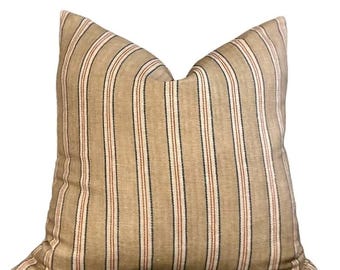 May include: A square decorative pillow with a tan background and vertical stripes in red, black, and white. The pillow has a soft, textured appearance and is likely made of fabric. The pillow is a home decor item.