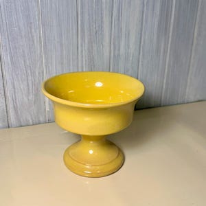 Peut inclure: Un bol sur pied en céramique jaune vif avec une finition lisse et brillante. Le bol présente un bord large et évasé qui se rétrécit vers une base circulaire robuste. La surface présente un vernis jaune éclatant et uniforme sur l'ensemble.