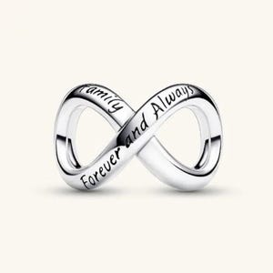 May include: A polished silver infinity charm featuring the engraved black text Family Forever and Always along the curved surface. The metallic piece has a smooth, reflective finish and a continuous looped design that forms a figure-eight shape.