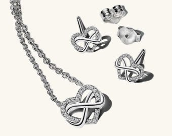 Puede incluir: Un conjunto de joyería de plata que consta de un collar y dos pendientes. Cada pieza presenta un diseño en forma de corazón integrado con un símbolo de infinito, incrustado con pequeñas piedras claras. El collar incluye una cadena fina.