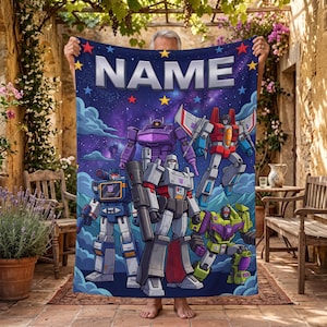 Könnte beinhalten: Eine rechteckige Fleecedecke mit einem dunkelvioletten Galaxie-Hintergrund und dem Wort NAME in großen weißen Buchstaben oben. Das Design zeigt fünf bunte Roboterfiguren in verschiedenen Posen, akzentuiert durch kleine gelbe und rote Sterne.