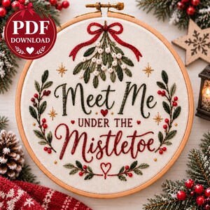 Può includere: Un telaio da ricamo circolare in legno contenente tessuto bianco con ricamo natalizio fatto a mano. Il design presenta vischio verde con bacche bianche, agrifoglio rosso e stelle dorate. Il testo ricamato recita Meet Me UNDER THE Mistletoe.