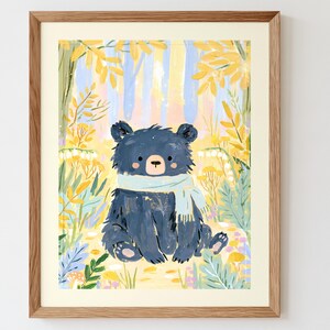 Peut inclure: Une impression d'art encadr&eacute;e repr&eacute;sentant un ours bleu fonc&eacute; portant une &eacute;charpe bleu clair, assis dans une for&ecirc;t avec un feuillage jaune et vert, des fleurs blanches et des tons pastel doux. L'&oelig;uvre est dans un cadre en bois clair.