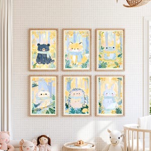 Peut inclure: Un ensemble de six cadres muraux illustrant un ours, un renard, une grenouille, un hibou, un h&eacute;risson et un lapin. Chaque animal est repr&eacute;sent&eacute; dans une for&ecirc;t aux tons jaunes et bleus, portant une &eacute;charpe bleu clair et entour&eacute; de feuillage.