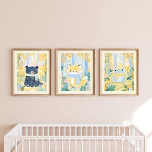 Peut inclure: Trois cadres muraux pr&eacute;sentant des illustrations &agrave; l'aquarelle d'un ours noir avec une &eacute;charpe bleue, d'un renard avec une &eacute;charpe bleue et d'une grenouille avec une &eacute;charpe jaune, sur un fond de feuillage forestier jaune et bleu.