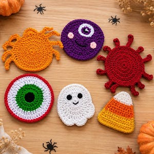 May include: Six crocheted coasters featuring Halloween themes: an orange spider, a purple cyclops, a red spiky creature, a green and white eyeball, a white ghost, and a yellow, orange, and white candy corn shape, all arranged on a wooden surface.