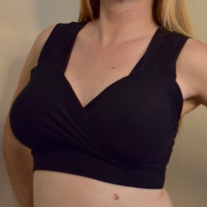 May include: A black, sleeveless, wrap-style top with a deep V-neckline. The top is made of a soft, stretchy fabric and has a cropped length.