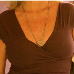 May include: A brown, v-neck, short-sleeved top with a triangular pendant necklace.