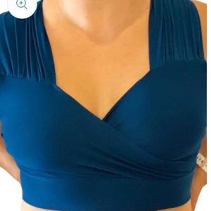 May include: A teal blue crop top with a deep V-neck and a criss-cross design in the front.