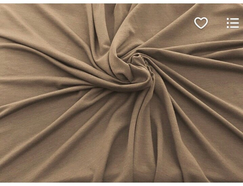 May include: A close-up shot of a fabric with a swirling pattern. The fabric is a solid, muted brown color. The material appears soft and drapes in folds, creating shadows and highlights.